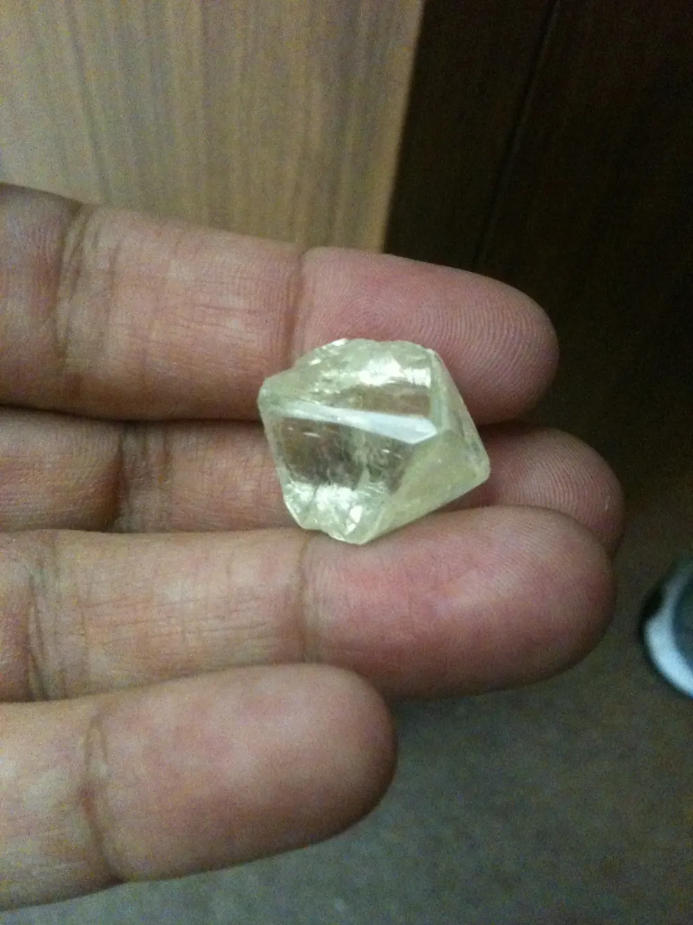 Diamant brut jaune clair de forme octaèdre tenu dans la main