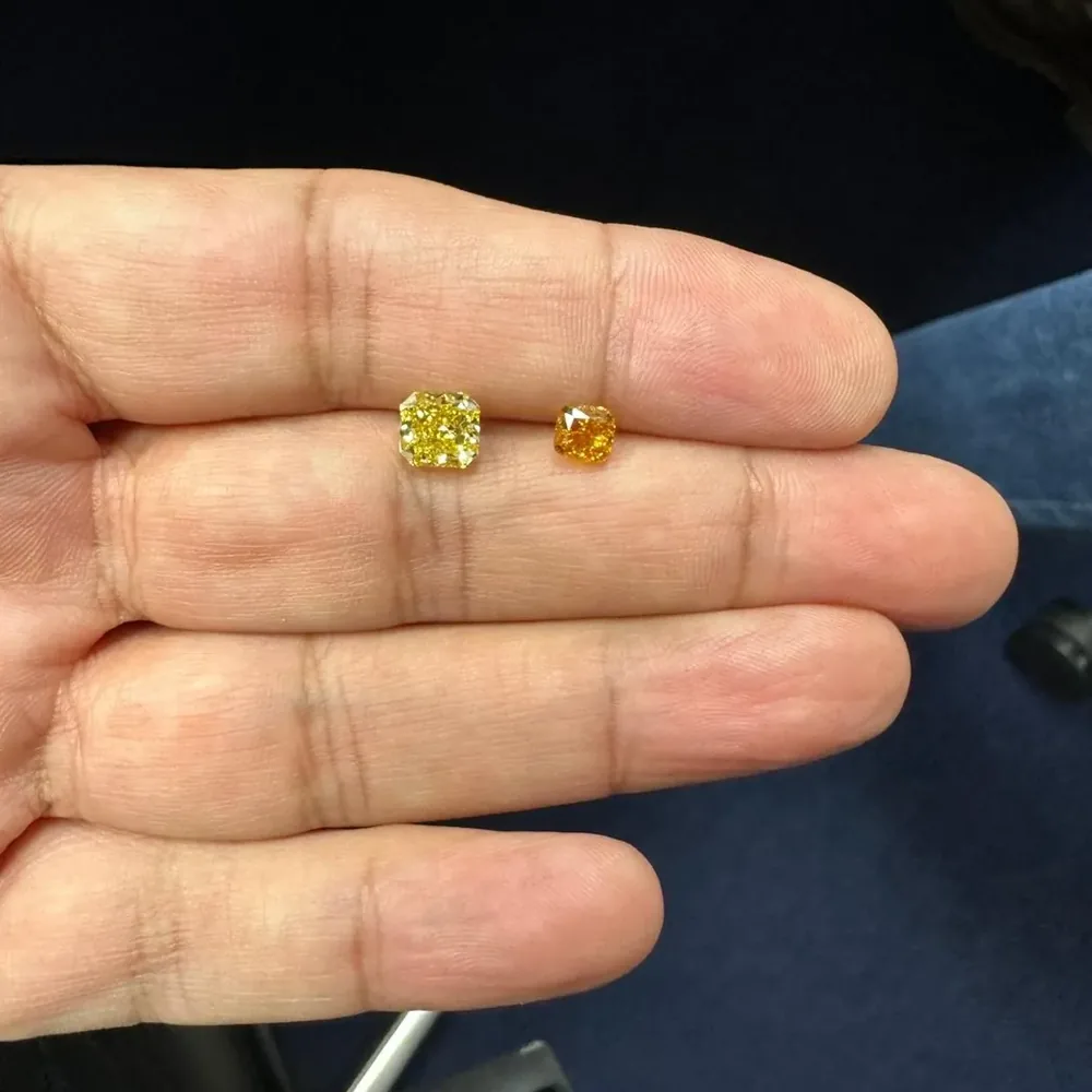 Deux petits diamants Fancy Colors jaune et orange, tenus entre les doigts